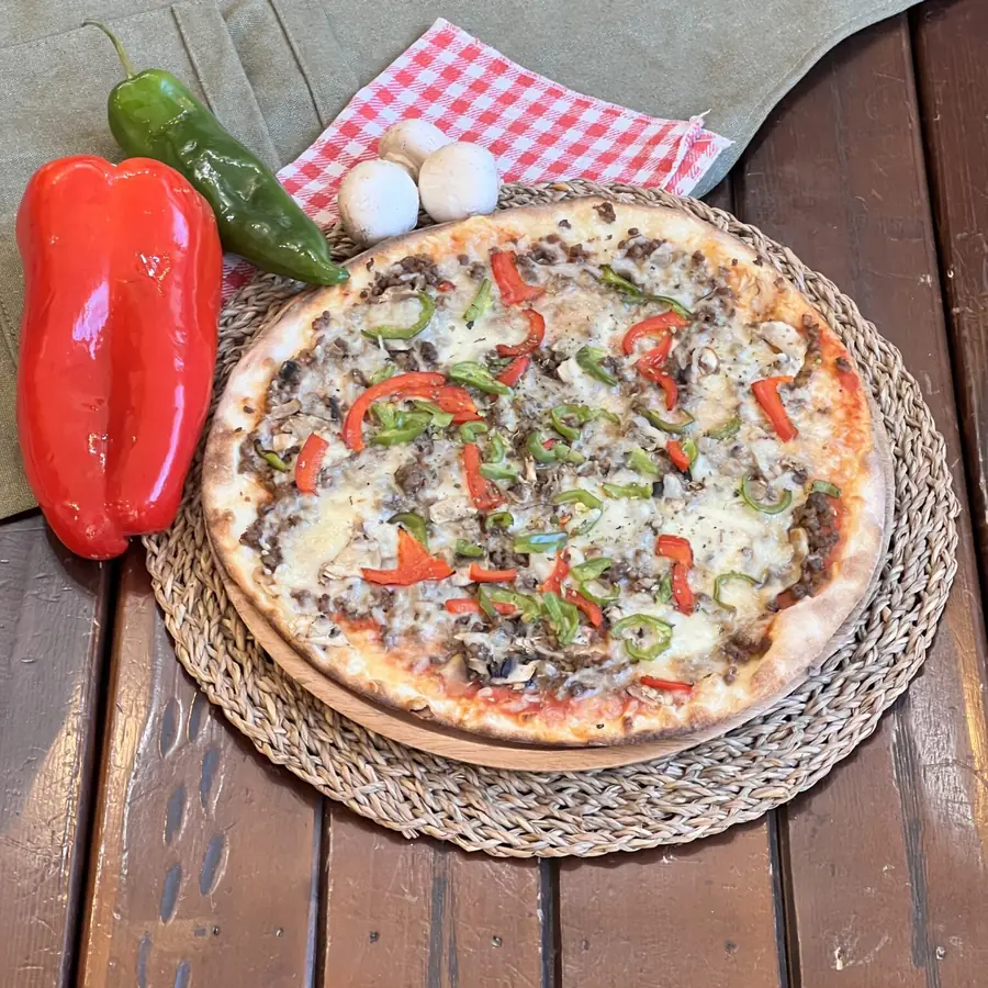 Pizza con carne y pimientos sobre mantel de cuadros